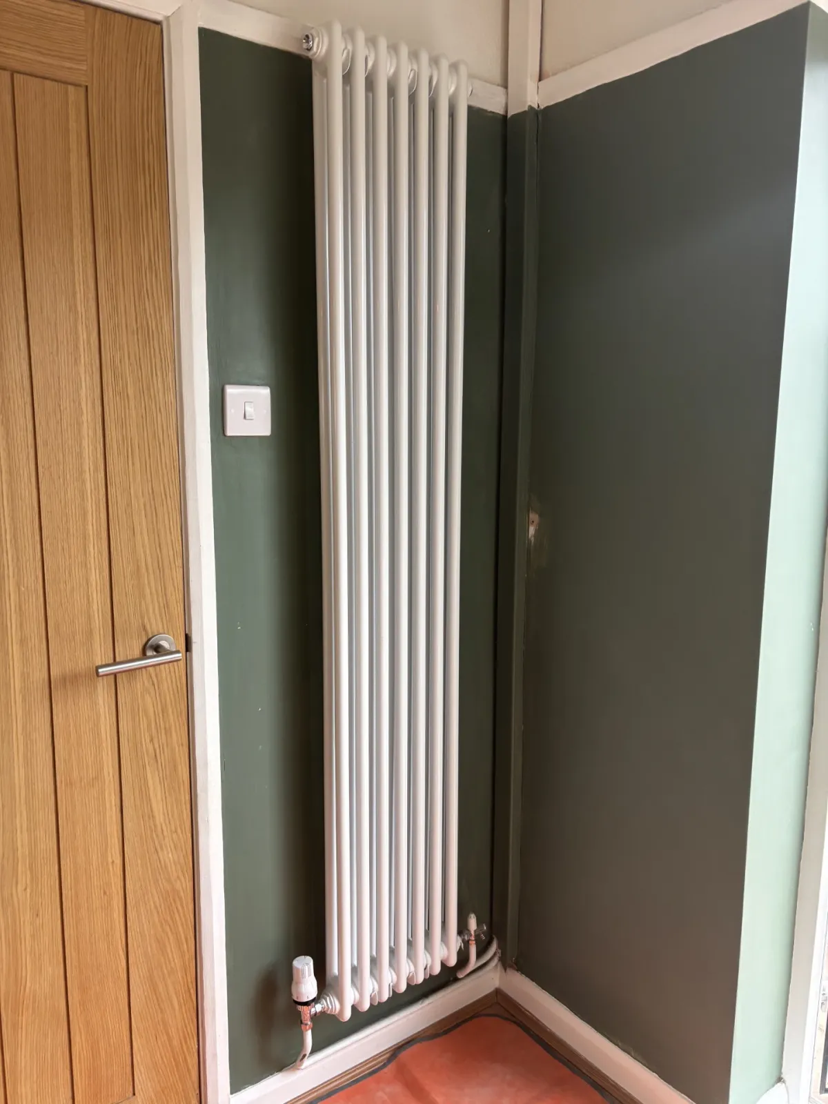Vertical column radiator fitted in a hallway nook with a thermostatic valve
